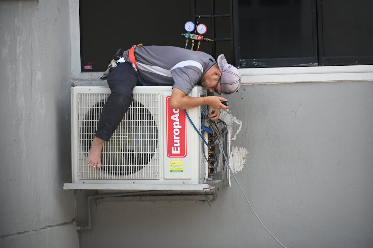 about-us A technician skillfully repairing an outdoor air conditioning unit mounted on a building wall.